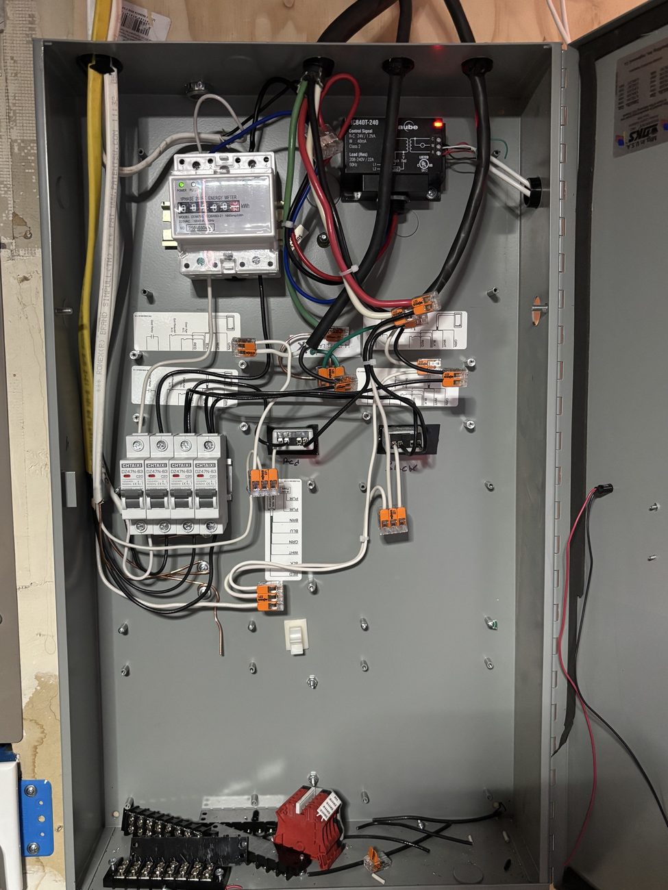 Open electrical control cabinet with breakers, meter, relays, and labeled wiring